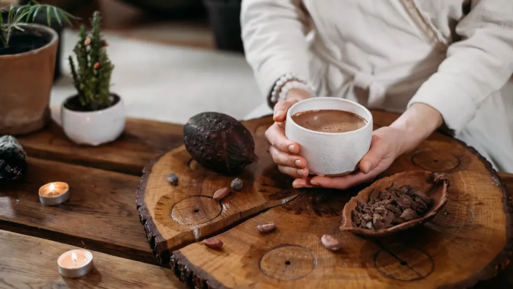 Whisking a ceremonial cacao drink with a wooden molinillo until frothy in a clay cup