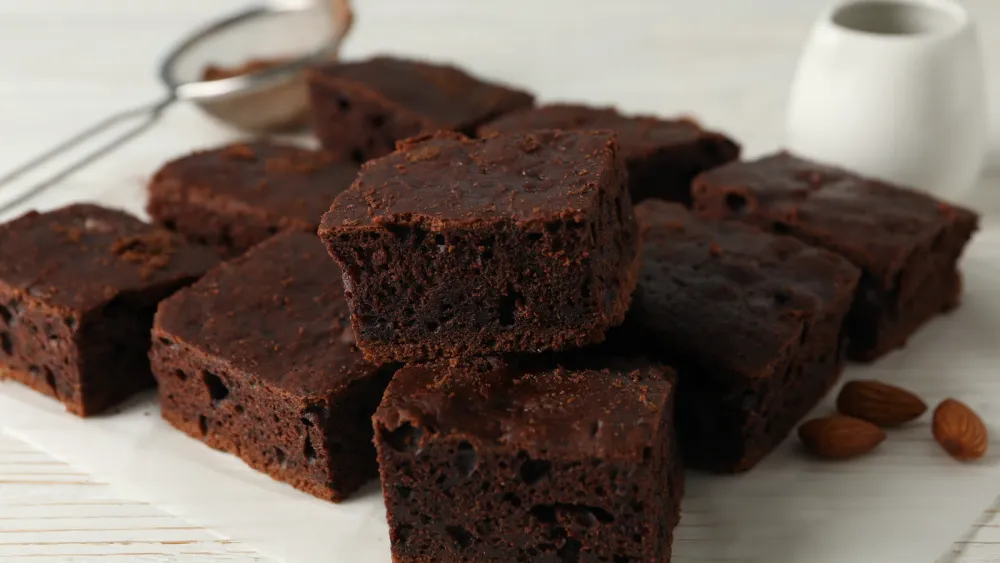Freshly baked keto brownies dusted with cocoa powder on a wire cooling rack, with bowls of cocoa powder and almond flour